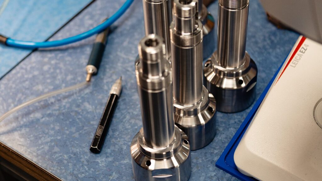 Pièces de précision en inox usinées par ARCOM Industrie, posées au poste de contrôle à côté du microscope